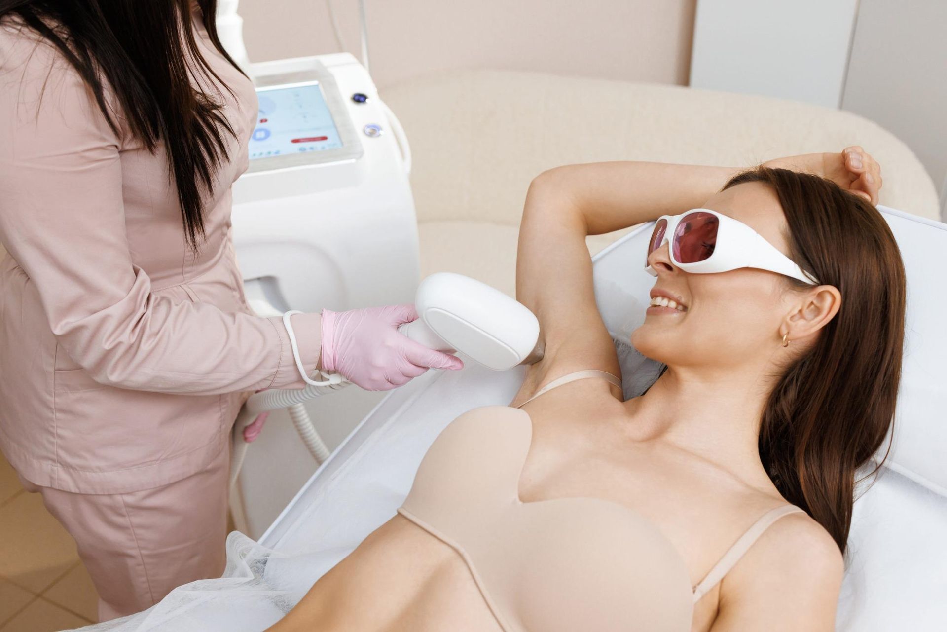 Una mujer recibe un tratamiento de depilación láser en una clínica, con gafas protectoras puestas.