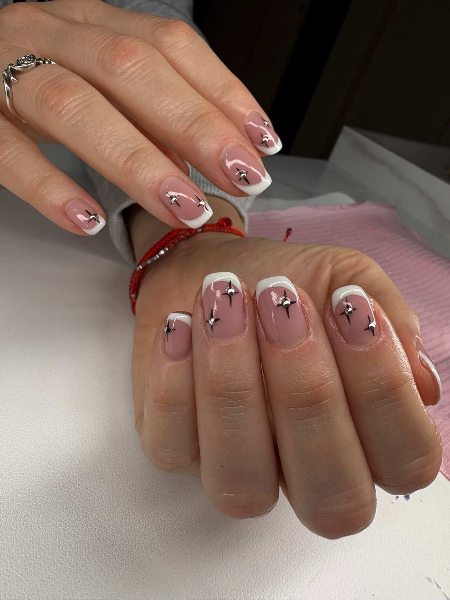 Primer plano de unas manos con uñas pintadas de rosa y blanco, descansando sobre una superficie blanca.