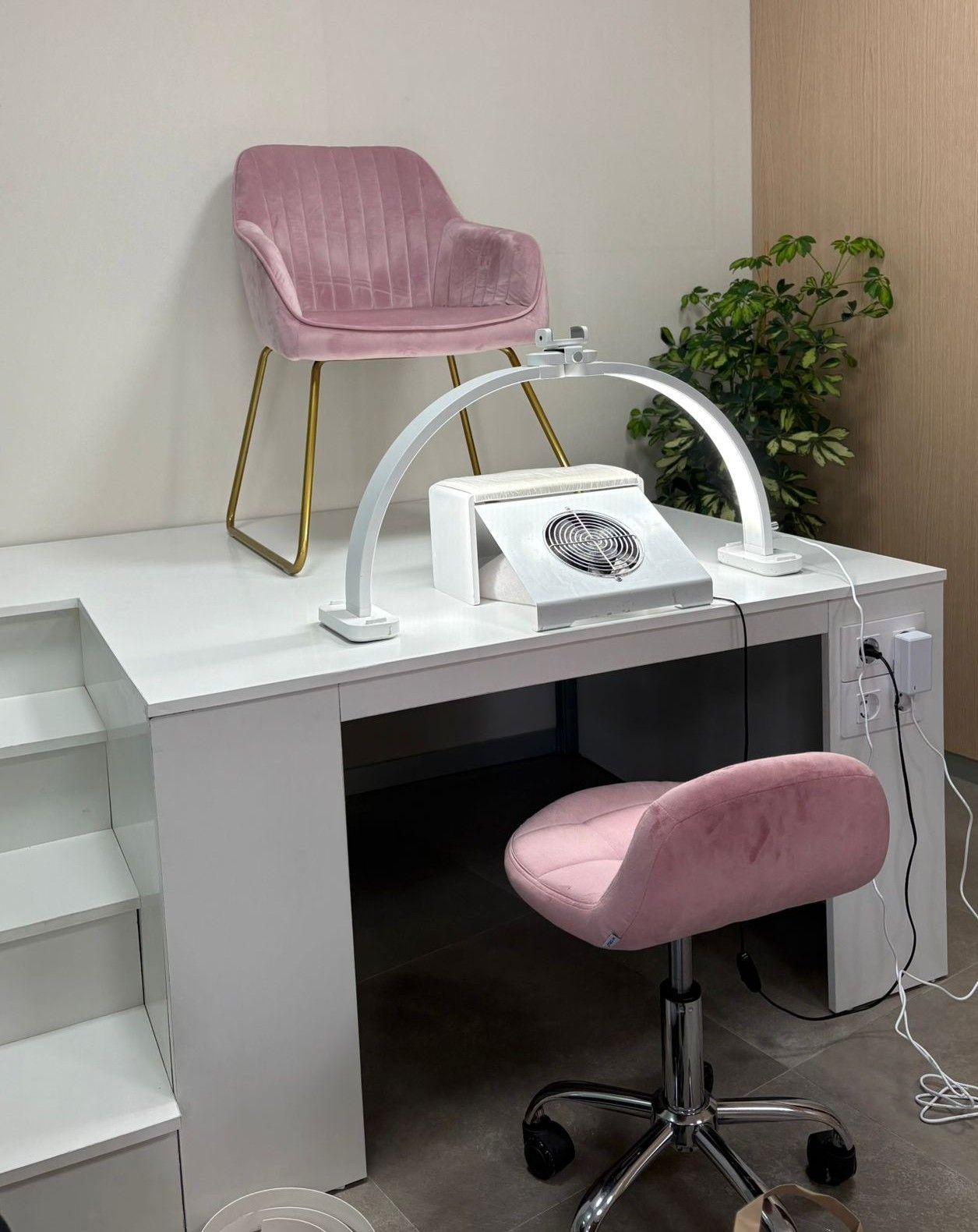 Estación de manicura rosa con silla, lámpara de escritorio y secador de uñas en una pequeña sala de belleza.