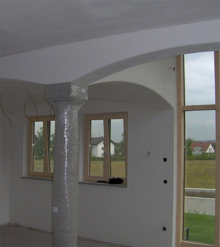 Ein im Bau befindlicher Innenraum zeichnet sich durch gewölbte Decken, eine zentrale Stützsäule und große Fenster mit Blick nach draußen aus.