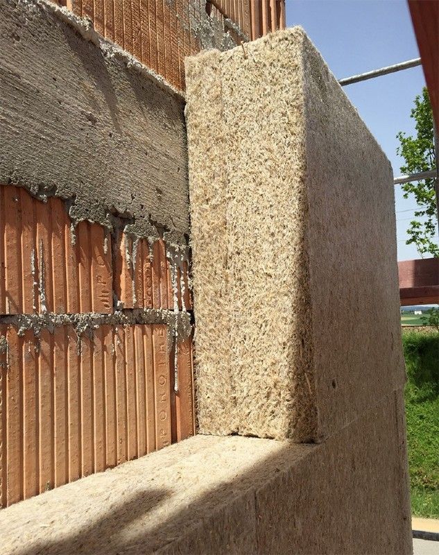An der Außenseite einer Ziegelwand auf einer Baustelle werden Dämmplatten aus Holzfasern angebracht.