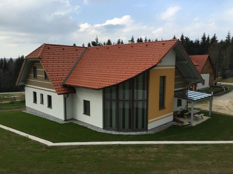 Ein modernes Haus mit rotem Ziegeldach, weißen und gelben Wänden und großen, bodentiefen Fenstern auf einem grasbewachsenen Hügel.