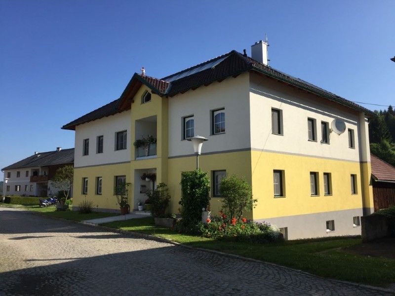 Ein zweistöckiges Gebäude mit gelbem Untergeschoss, weißem Obergeschoss und dunklem Spitzdach auf einer gepflasterten Auffahrt.