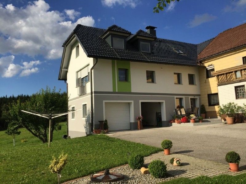 Ein zweistöckiges Haus mit weißer, grauer und grüner Außenfarbe, dunklem Dach und Garagentoren, neben einem Rasengarten.