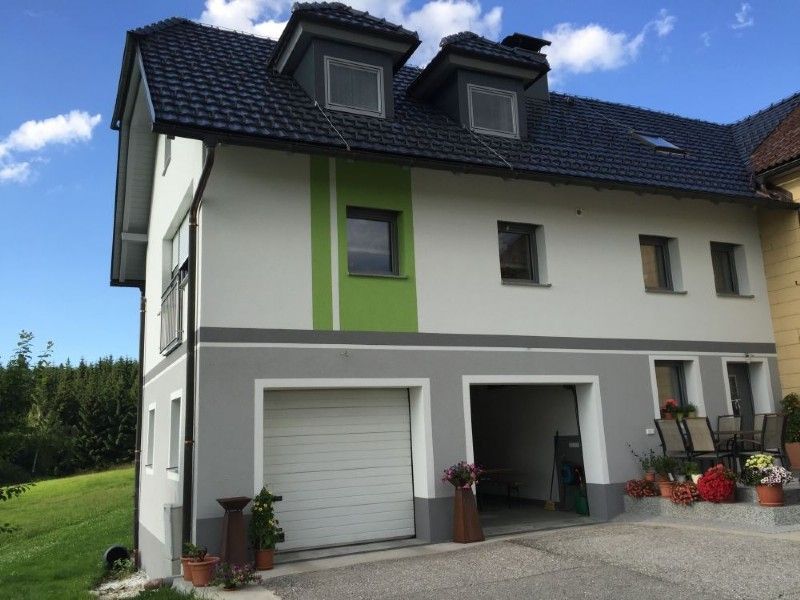 Zweistöckiges Haus mit weiß-grauer Fassade, einem limettengrünen Akzentpaneel, einer Garage und zwei Dachgauben.
