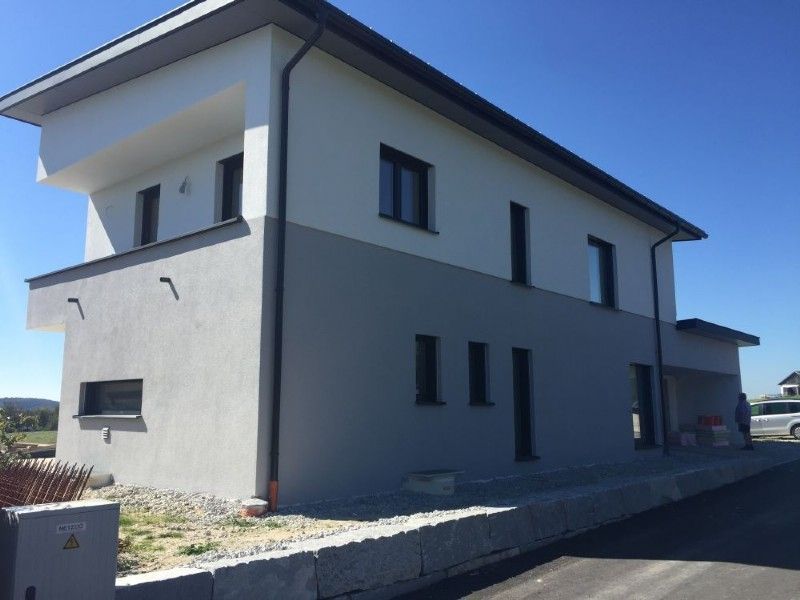 Ein modernes, zweistöckiges Haus mit weiß-grauer Fassade, Flachdach und Steingarten unter strahlend blauem Himmel.