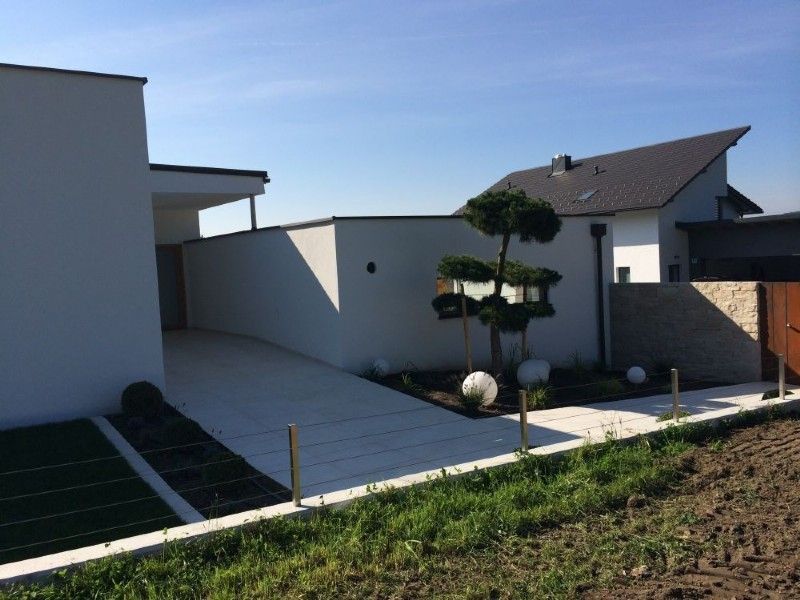 Modernes weißes Haus von außen mit gepflasterter Auffahrt, einem akkurat geschnittenen Formbaum und einer steinernen Akzentmauer an einem sonnigen Tag.