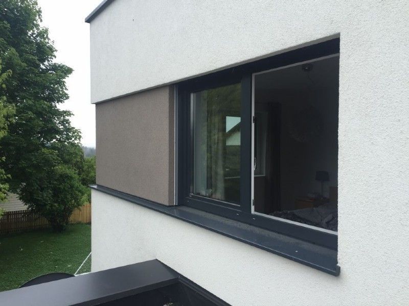 Ein teilweise geöffnetes Fenster mit dunklem Rahmen und grauer Seitenwand, eingelassen in eine weiße Außenwand.