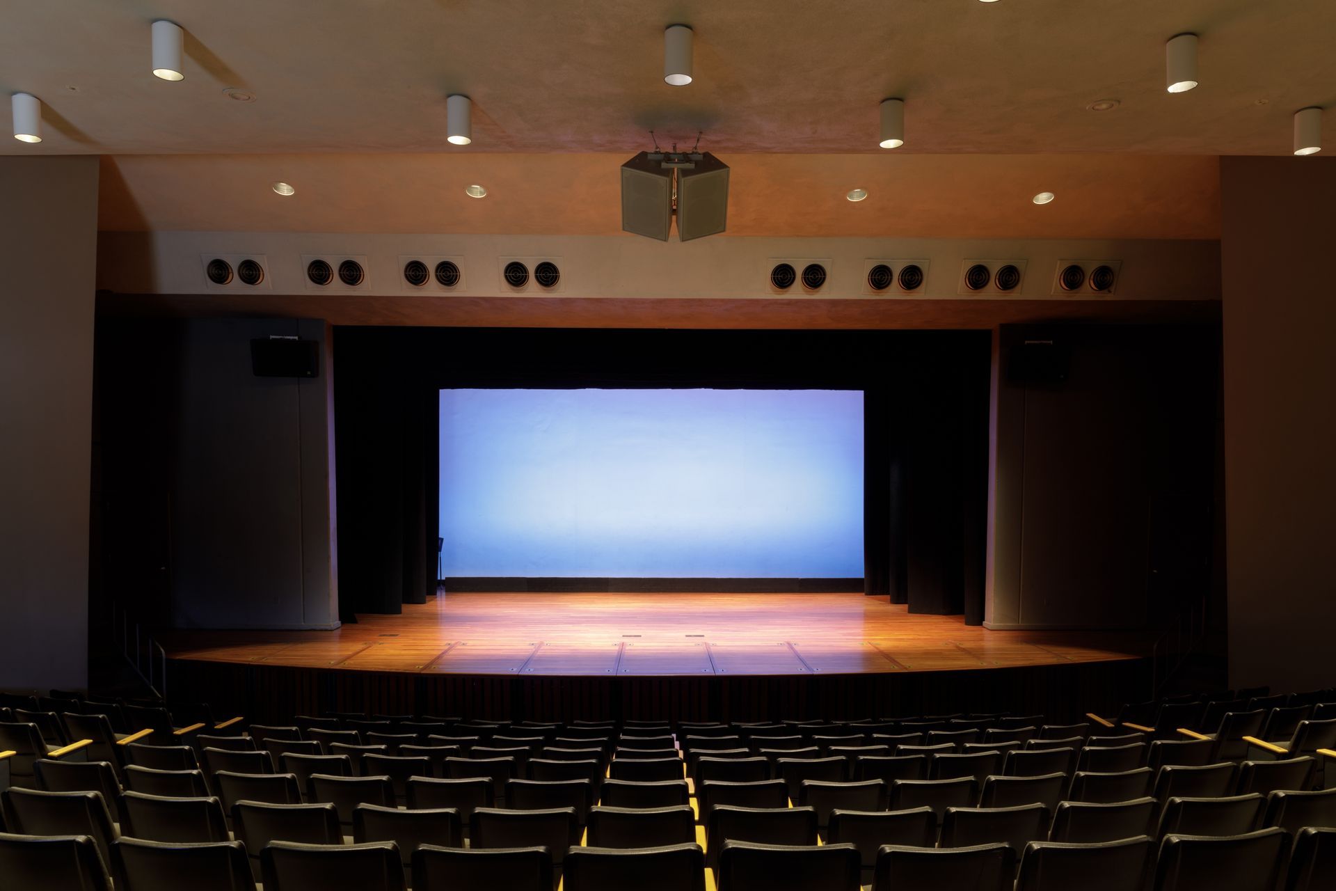 Théâtre vide avec des rangées de sièges faisant face à une scène éclairée et un grand écran.