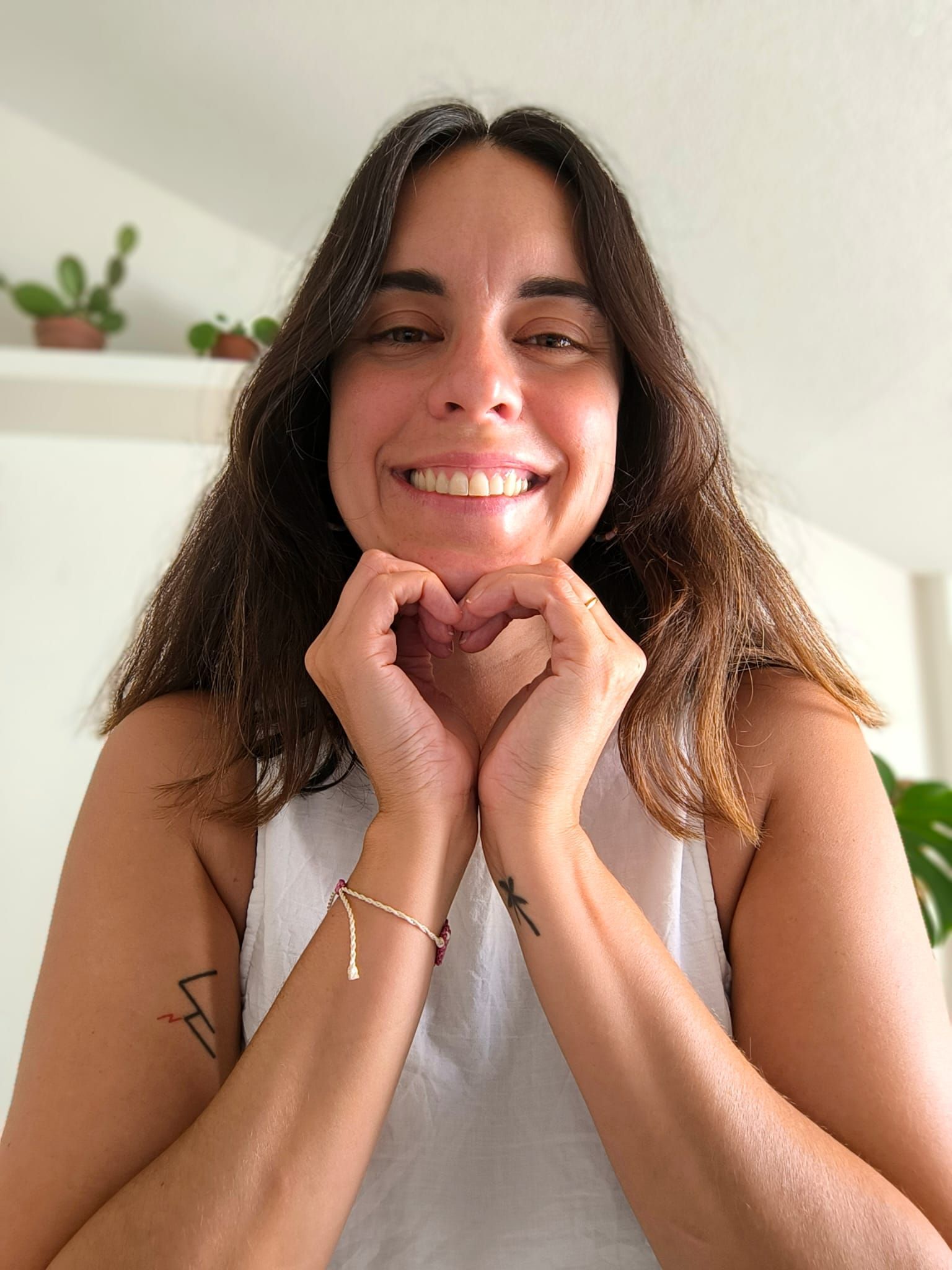 Persona sonriente con una blusa blanca con volantes sobre un fondo claro liso.