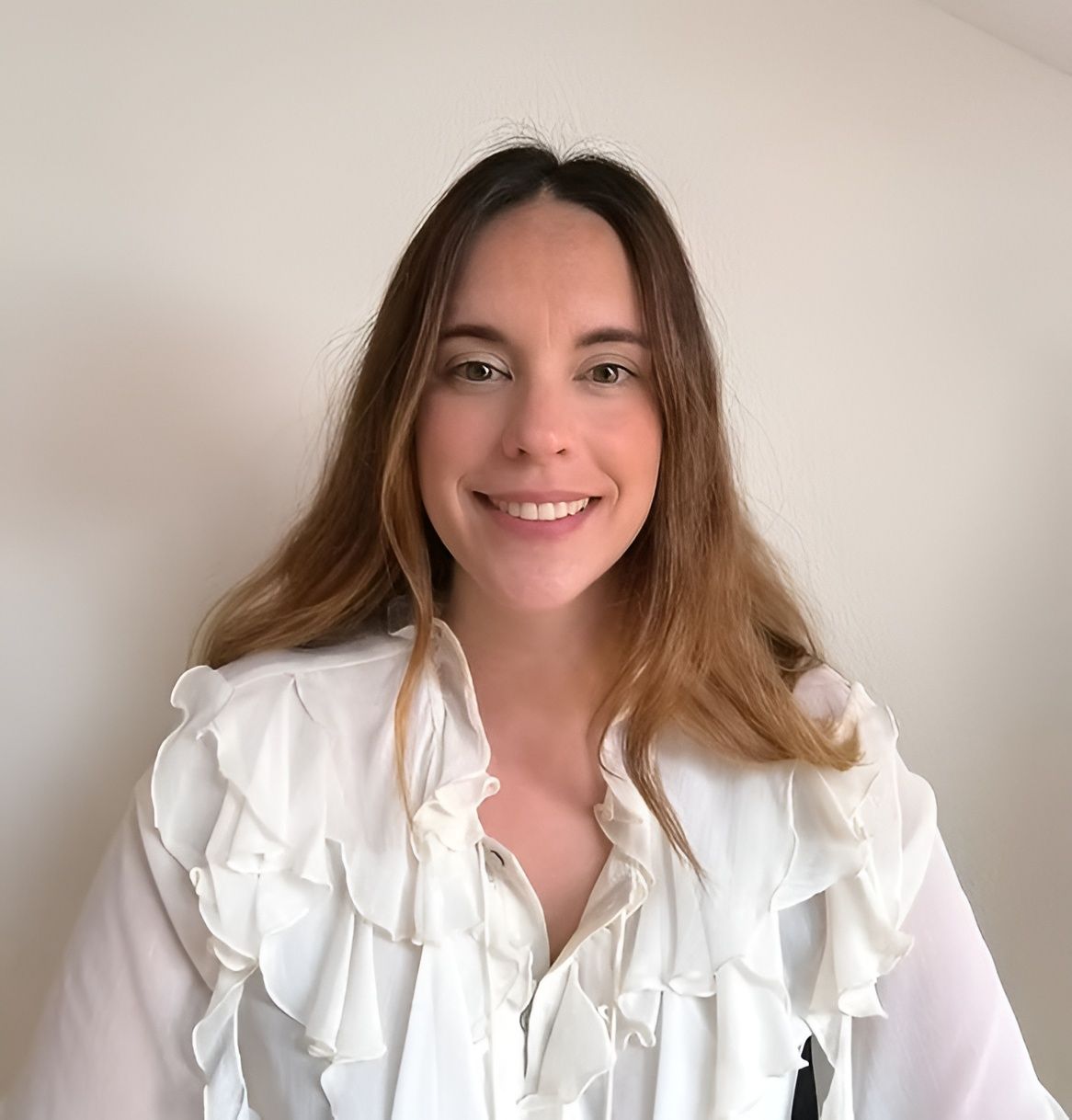 Persona sonriente con una blusa blanca con volantes sobre un fondo claro liso.