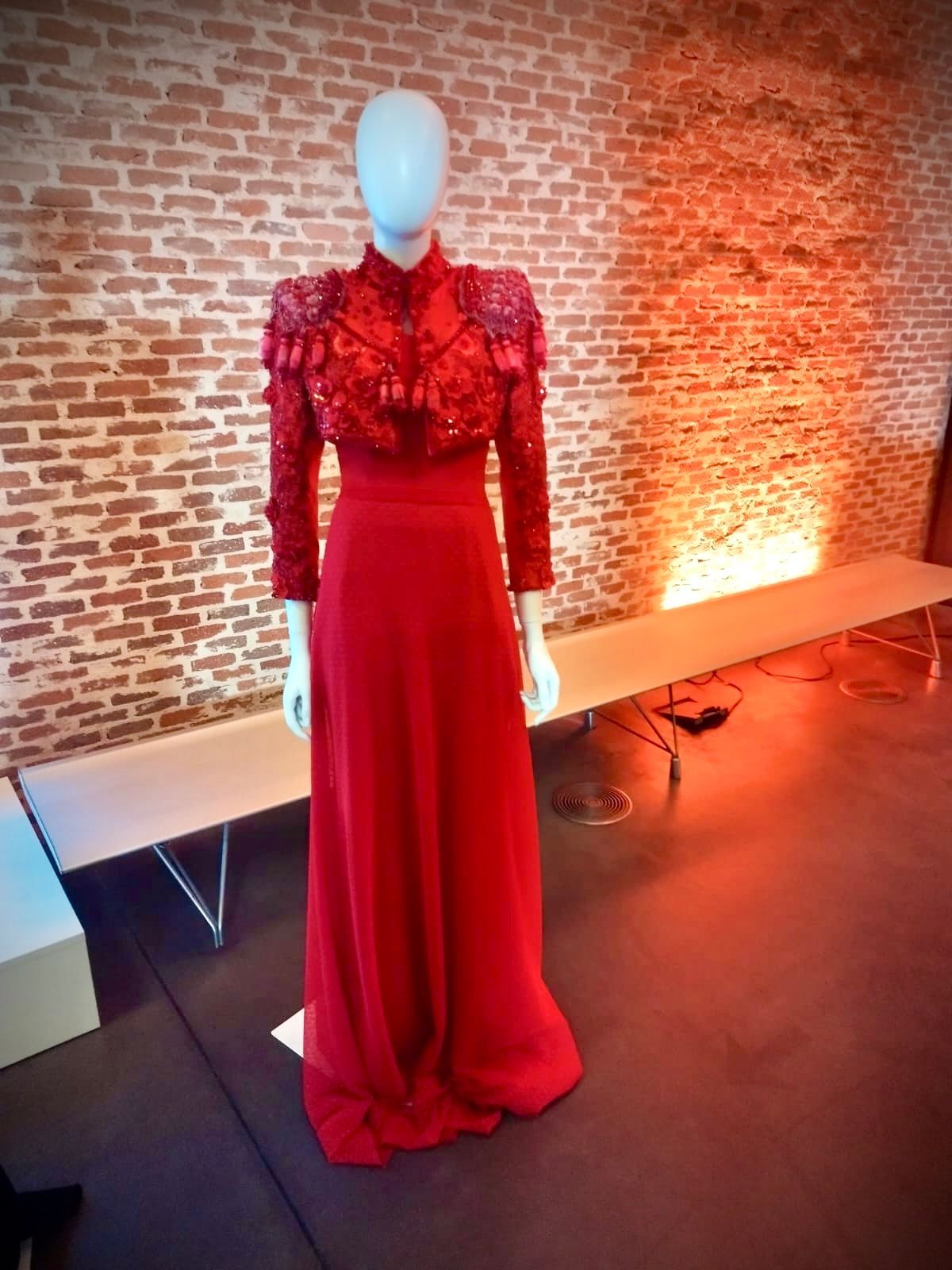 Un maniquí que lleva un vestido rojo está parado frente a una pared de ladrillos.