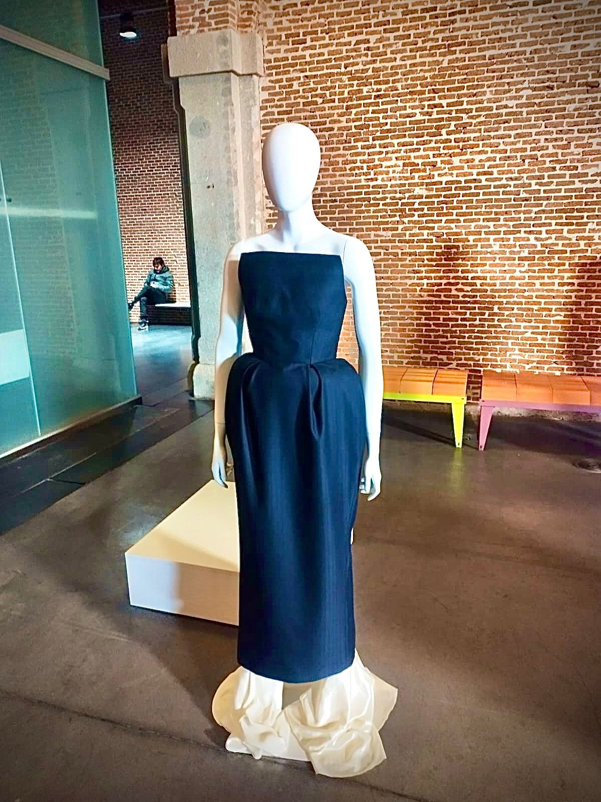 Un maniquí con un vestido negro está parado frente a una pared de ladrillos.