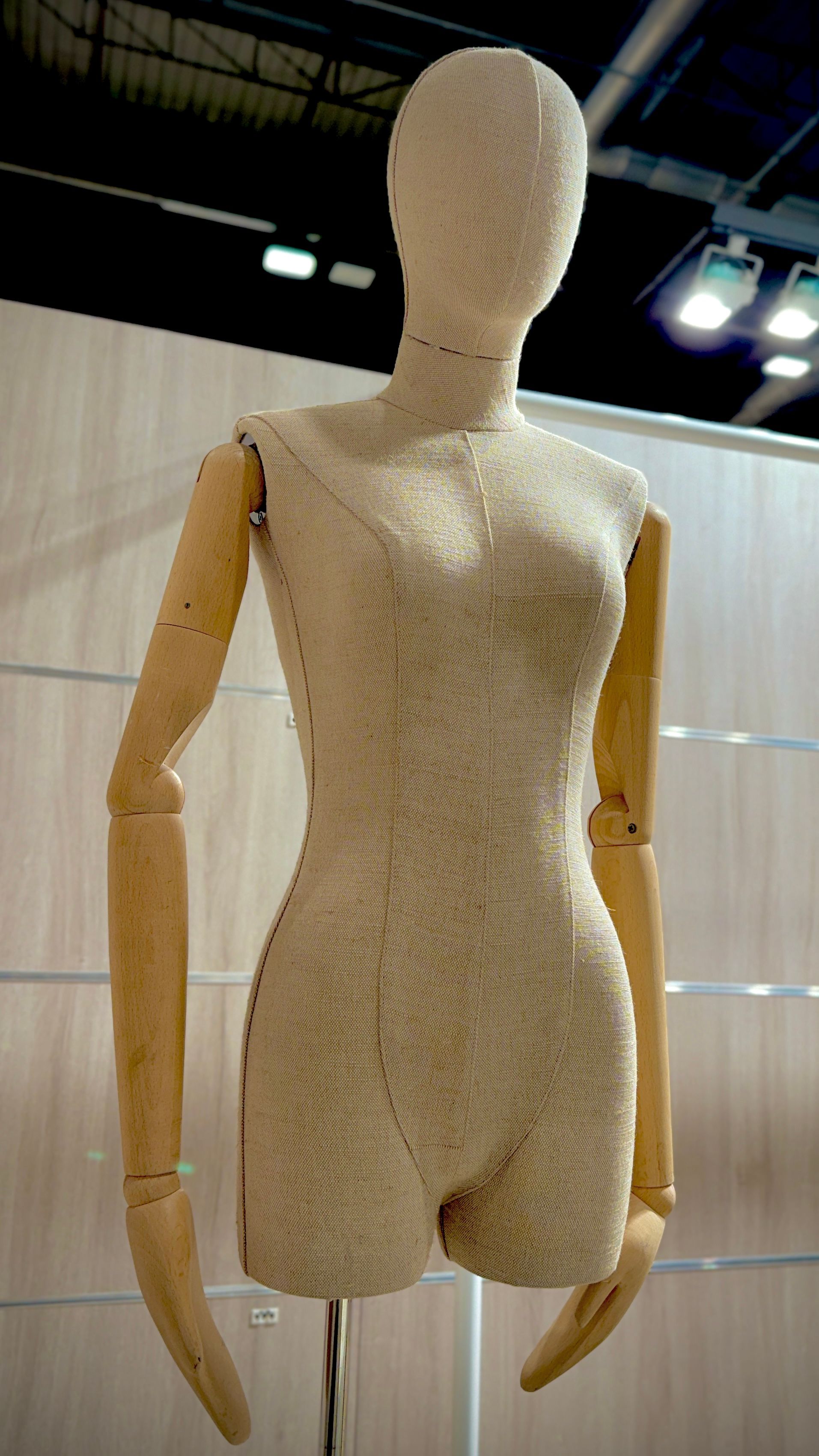 Un maniquí con brazos de madera está parado frente a una pared de madera.
