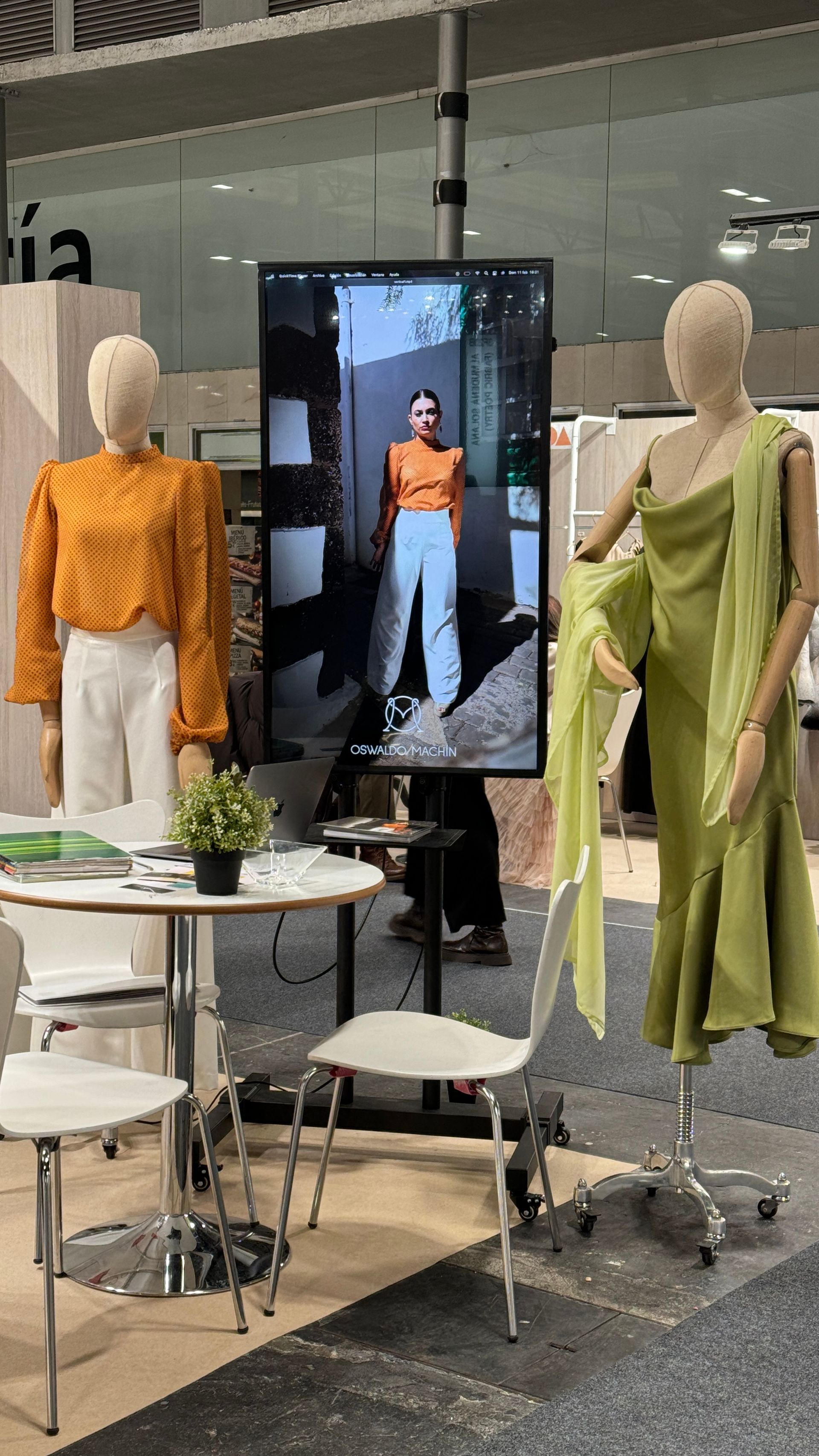 Un maniquí con un vestido verde está parado frente a una pantalla grande.