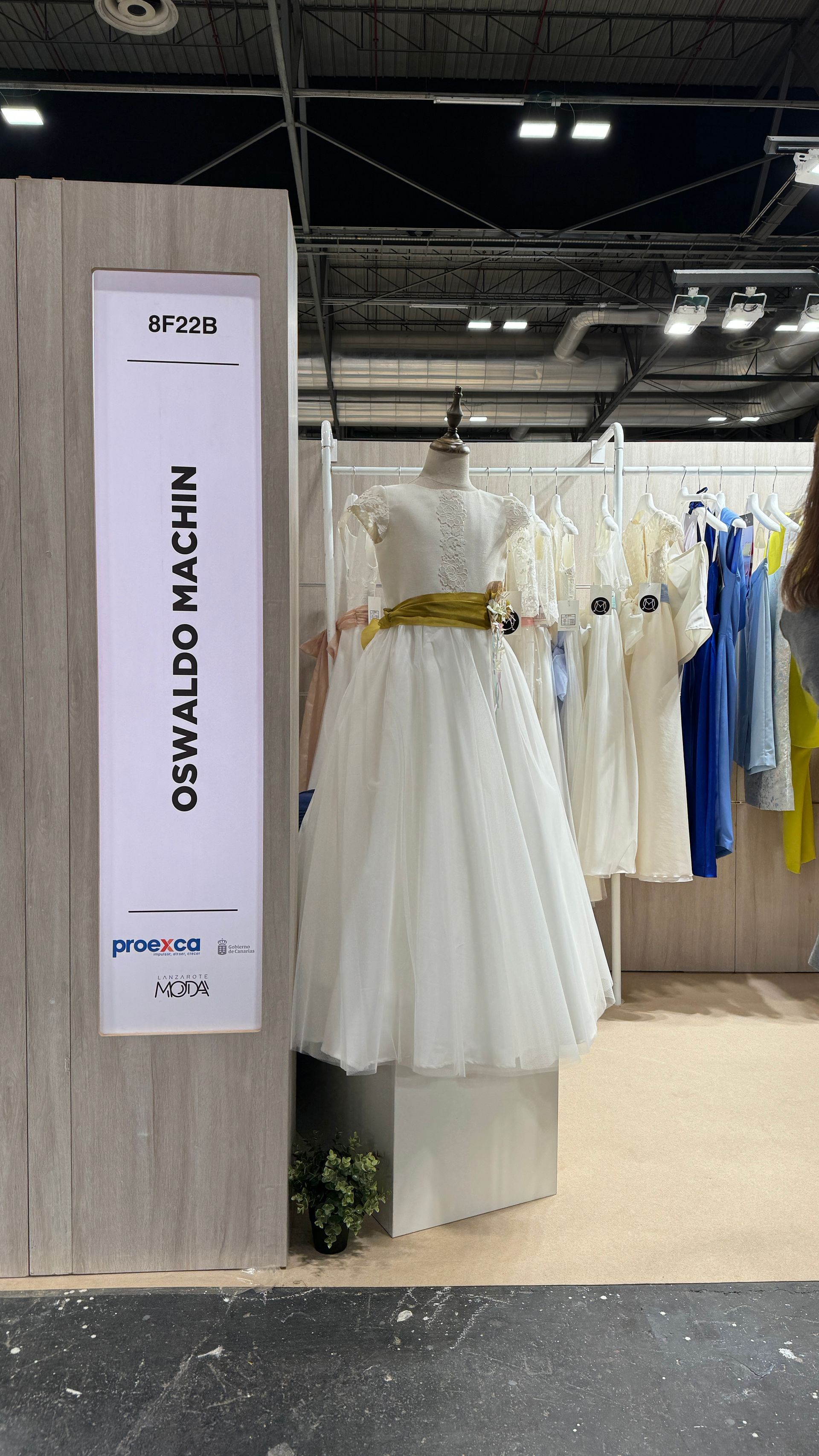 Un vestido blanco está sentado sobre un maniquí frente a un cartel que dice Oswaldo Machin.