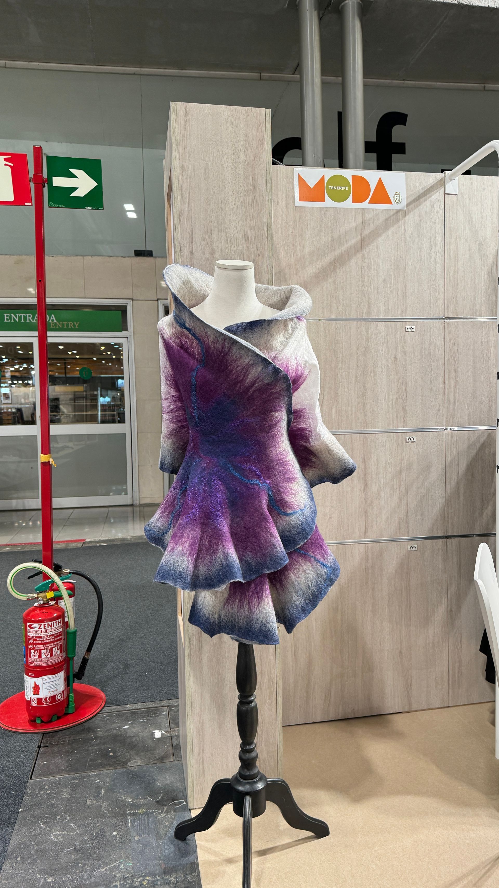 Un maniquí que lleva un vestido morado y azul está parado frente a un extintor de incendios.