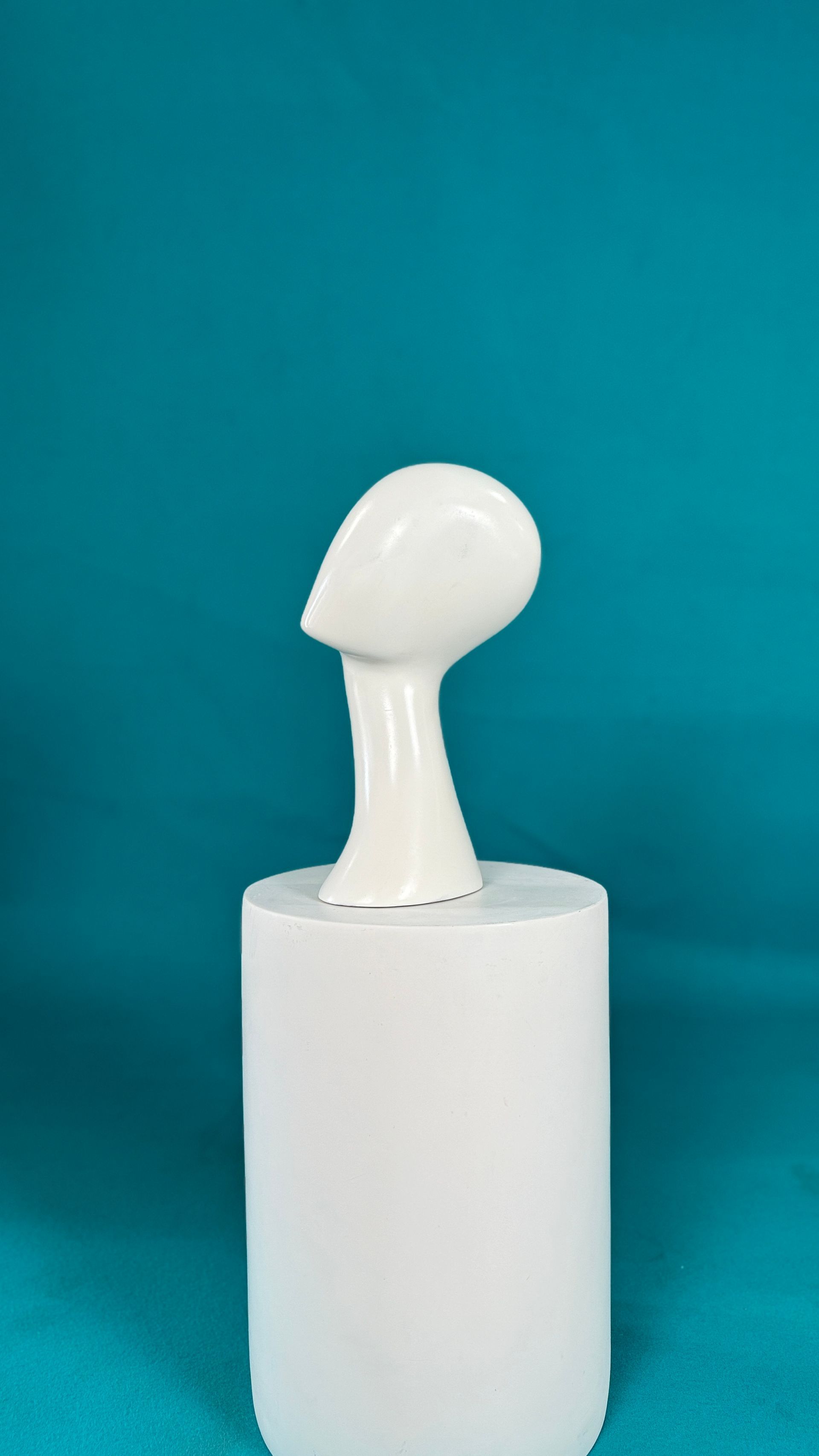 Una cabeza de maniquí blanca está sentada sobre un cilindro blanco sobre un fondo azul.