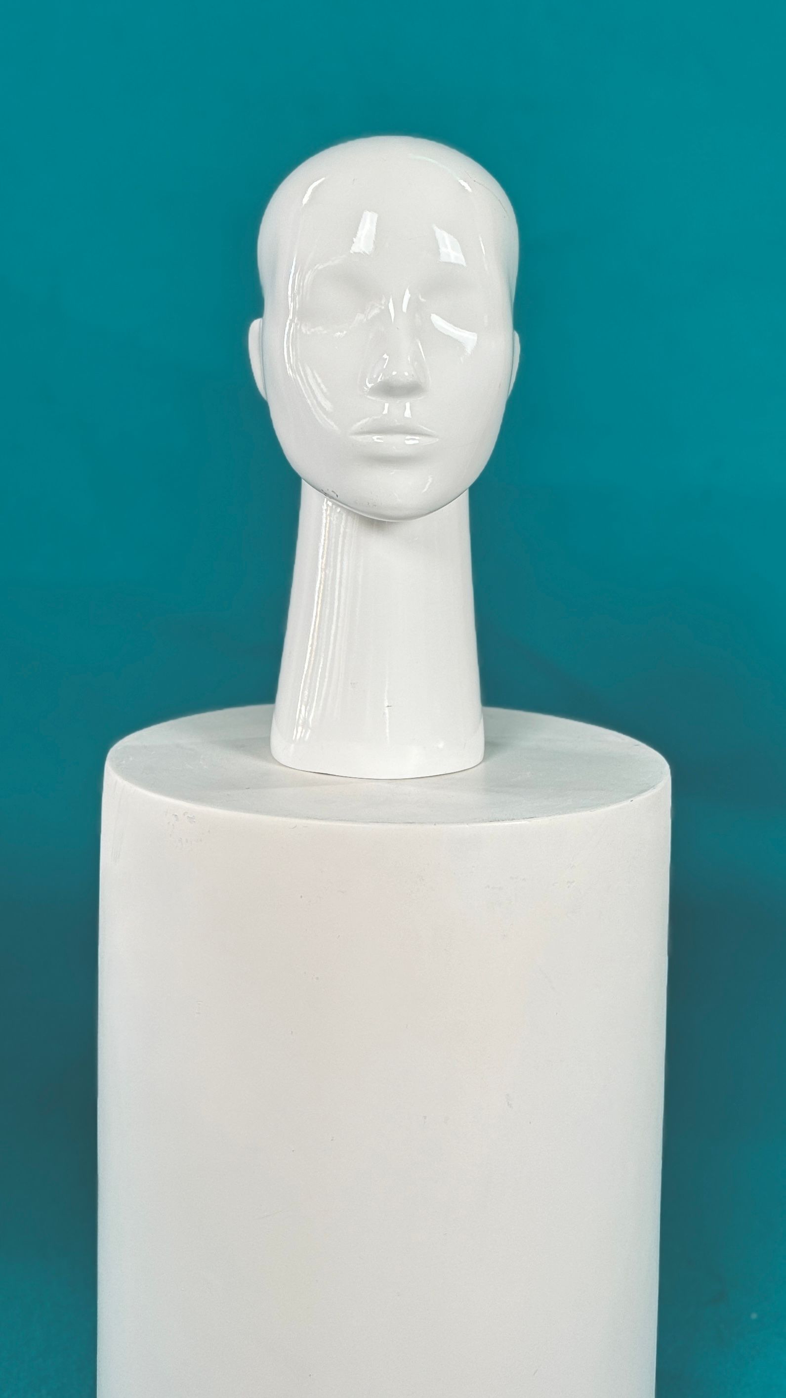 Una cabeza de maniquí blanca está sentada encima de un cilindro blanco.