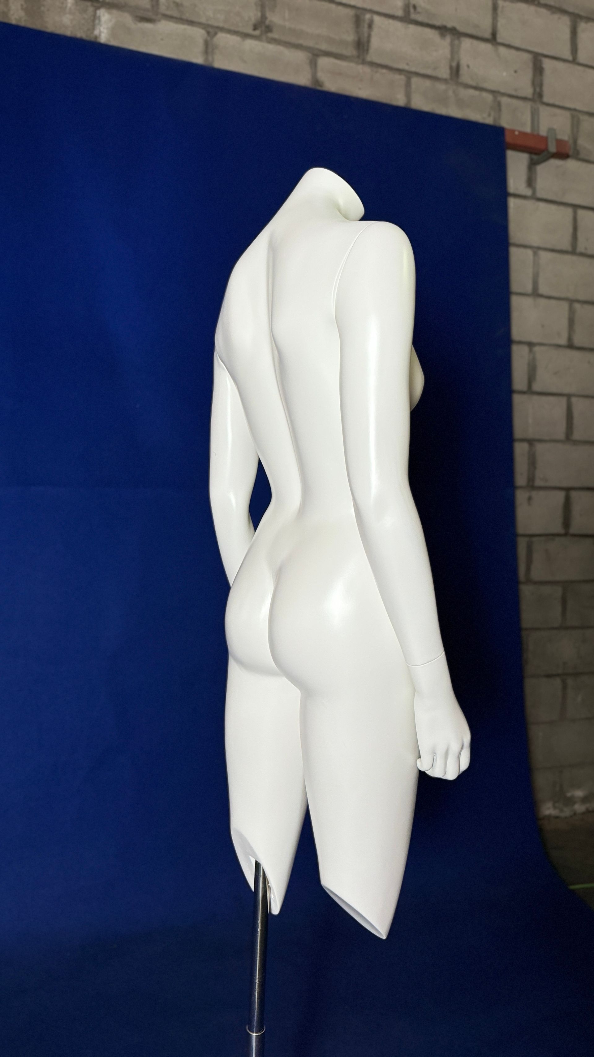 Un maniquí blanco sin cabeza está parado frente a una pared azul.
