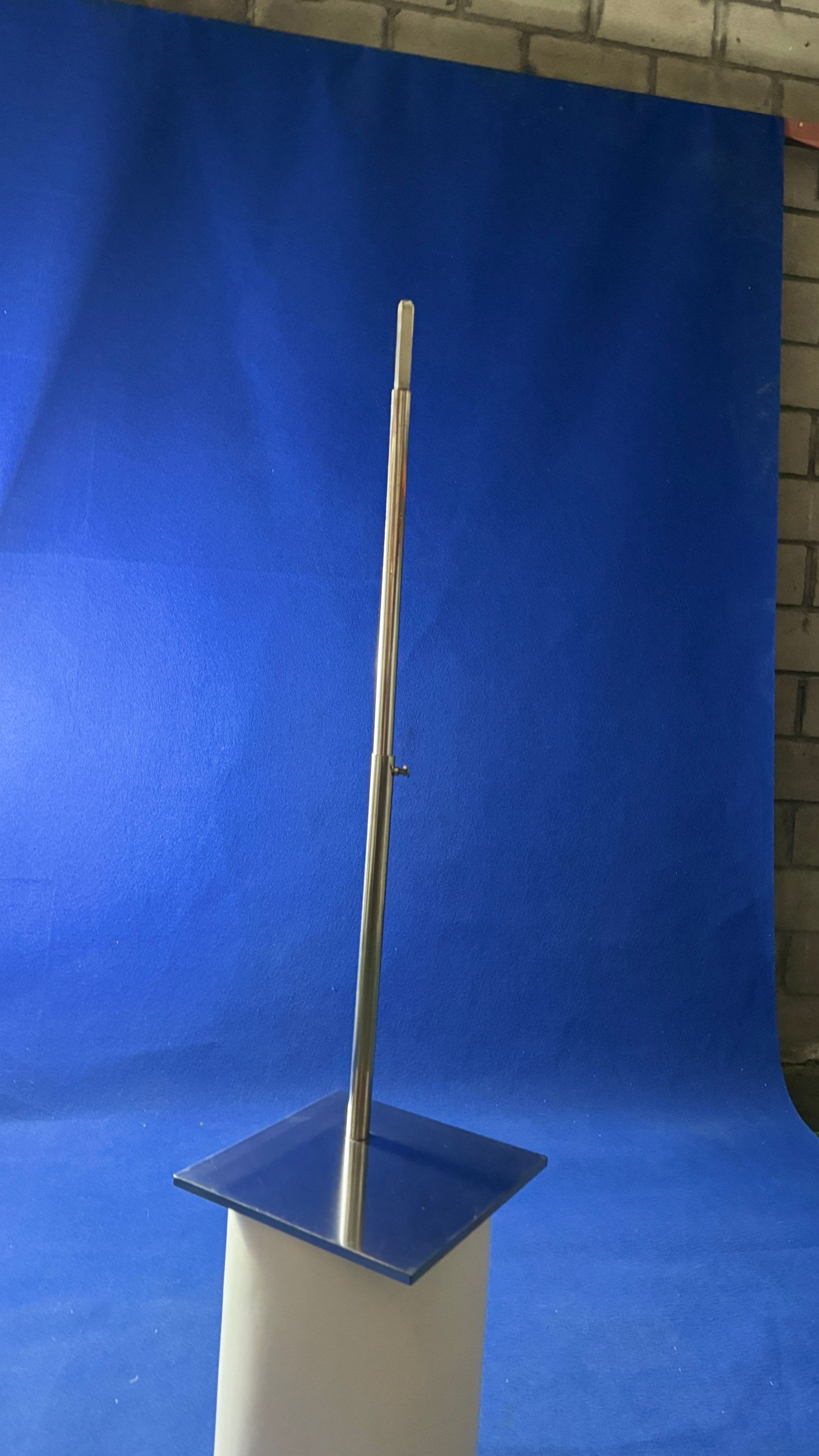 Una escultura de acero inoxidable se encuentra sobre un pedestal de vidrio frente a un fondo azul.