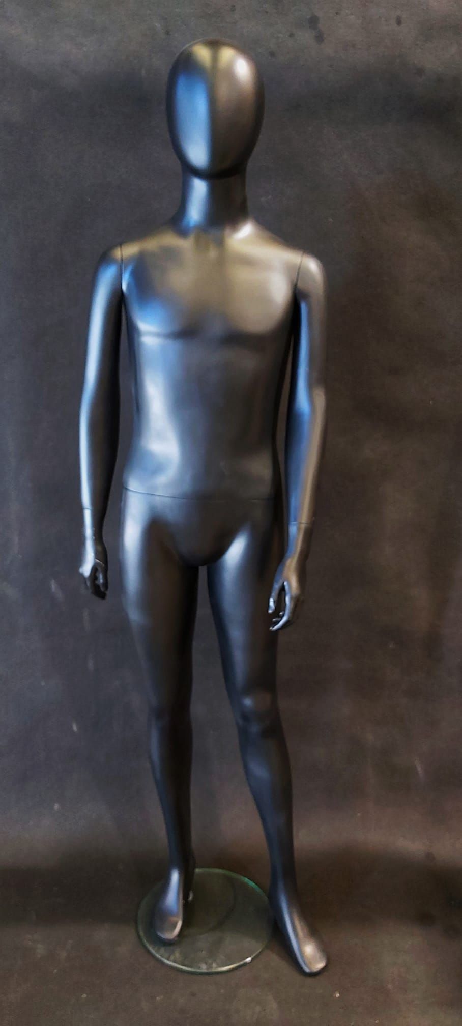 Un maniquí masculino negro está de pie sobre una base de vidrio.