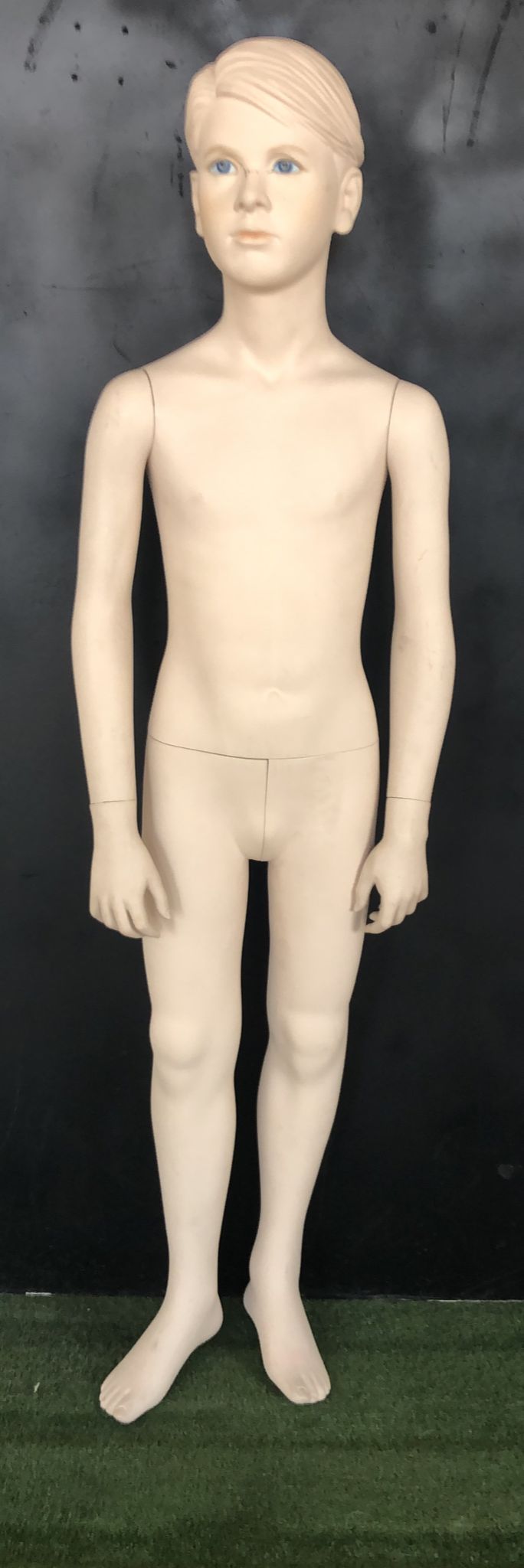 Un maniquí de niño pequeño está parado en un campo de hierba.