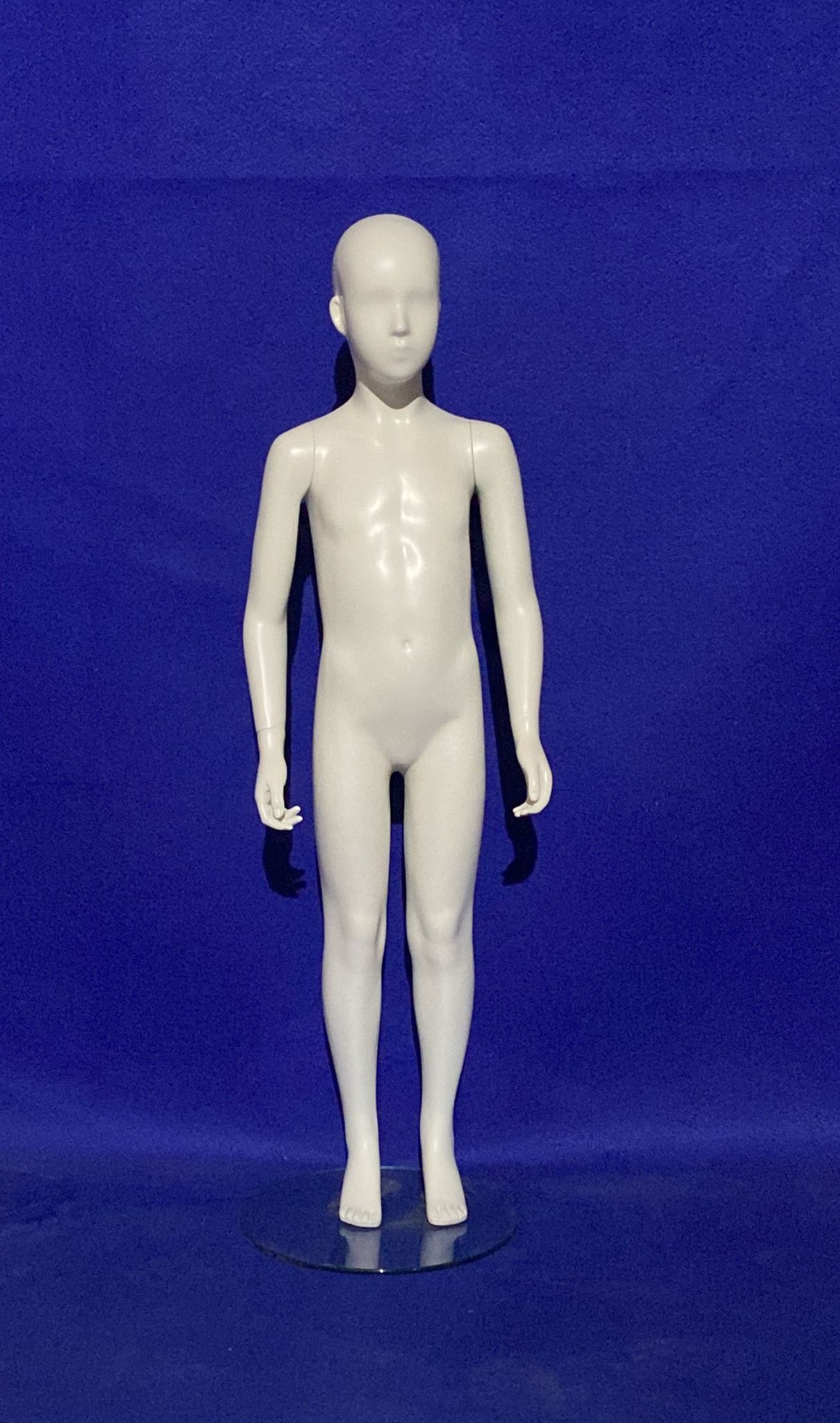 Un maniquí de niño blanco está de pie sobre una superficie azul.