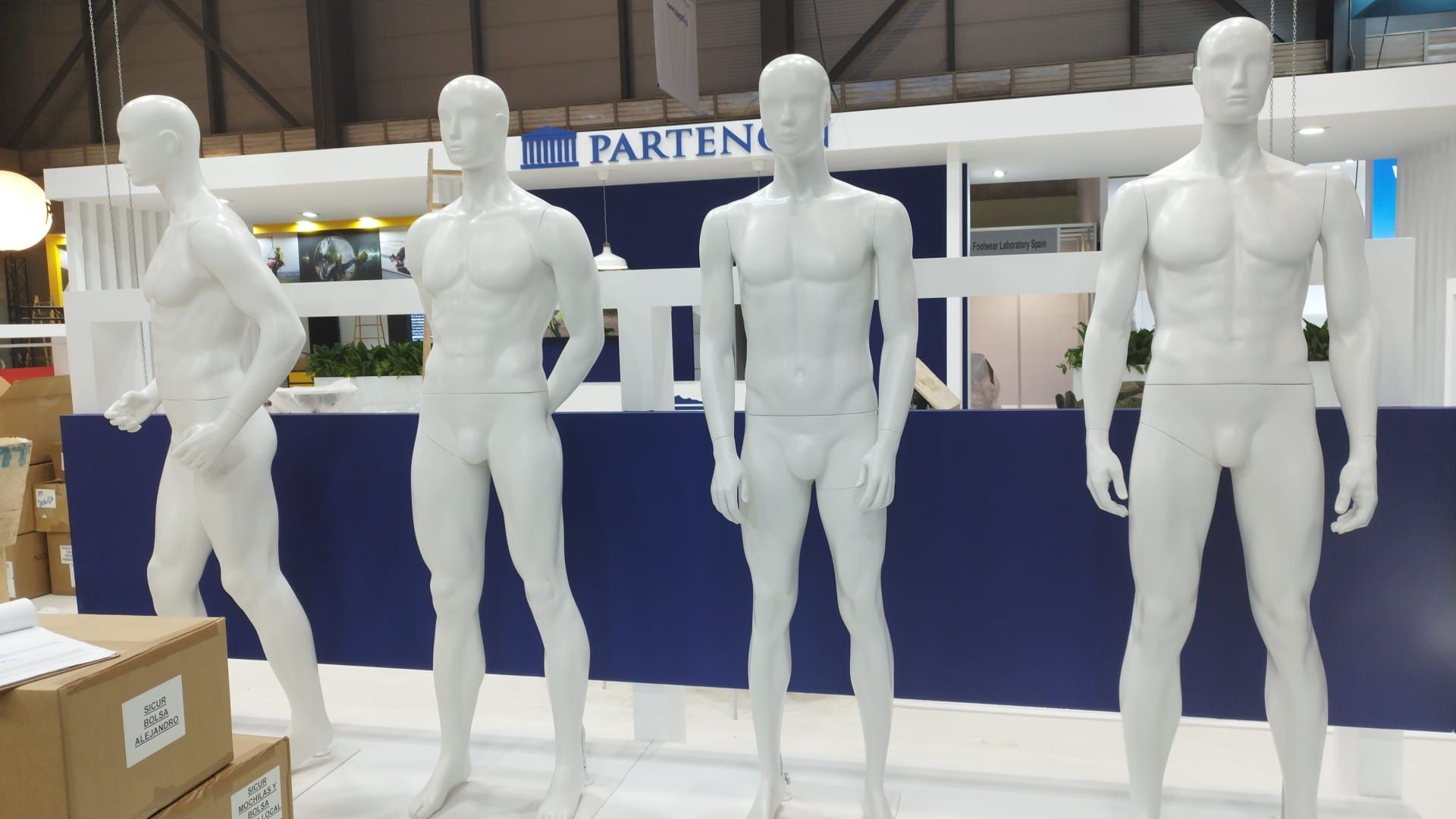 Cuatro maniquíes están de pie frente a un cartel que dice parteno