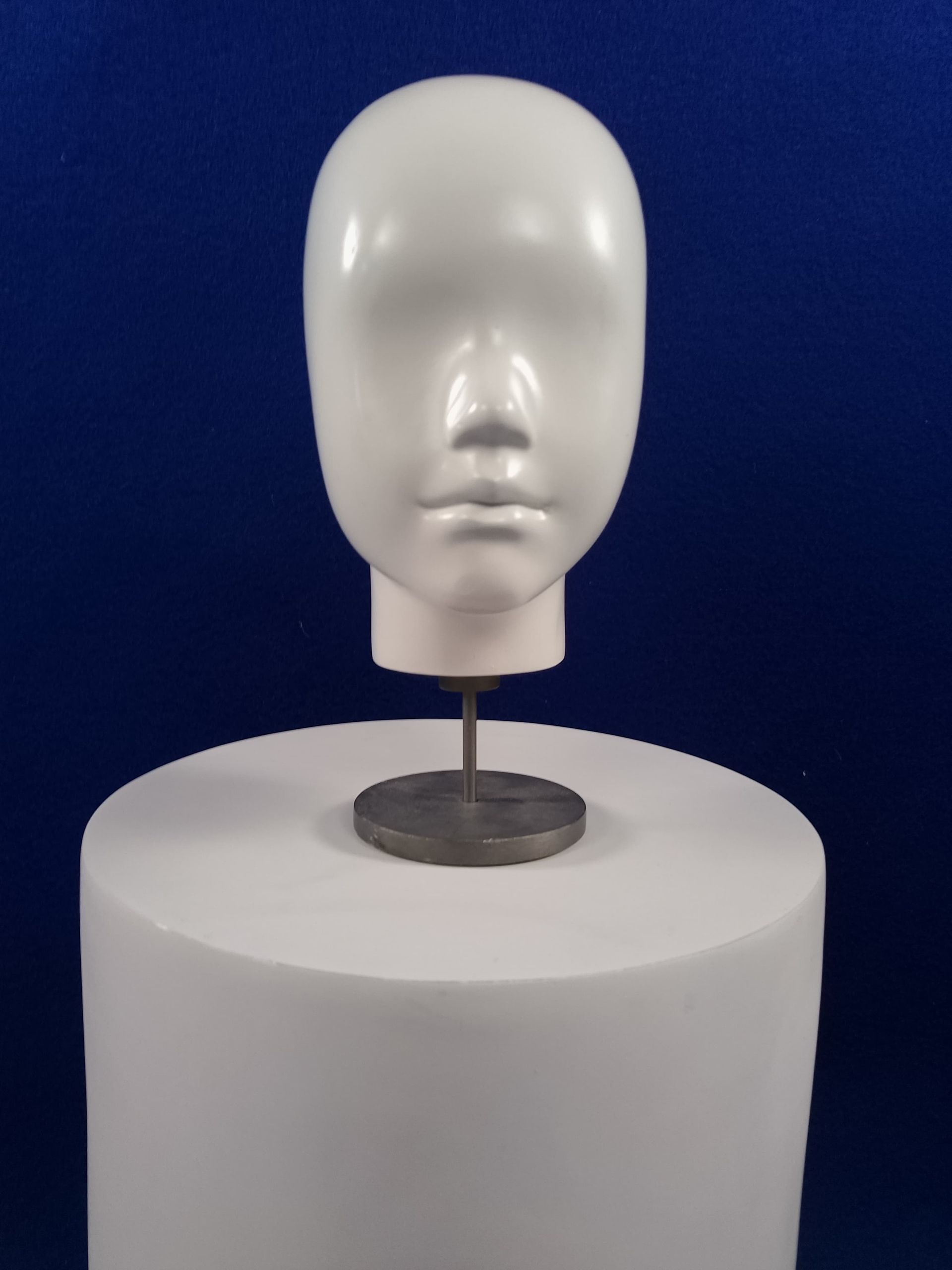 Una cabeza de maniquí blanca está sentada sobre un cilindro blanco.