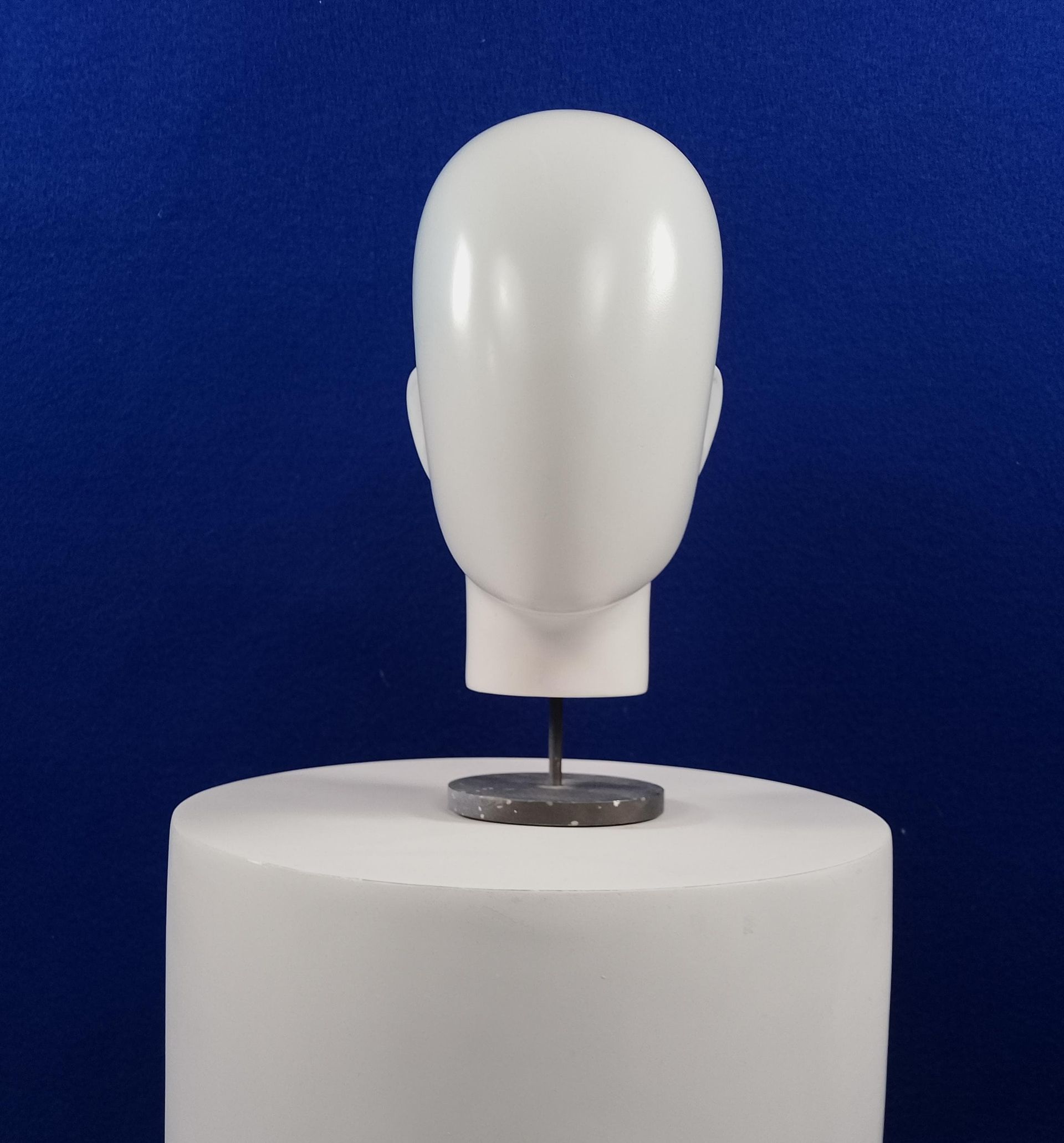 Una cabeza de maniquí blanca está sentada sobre un cilindro blanco.