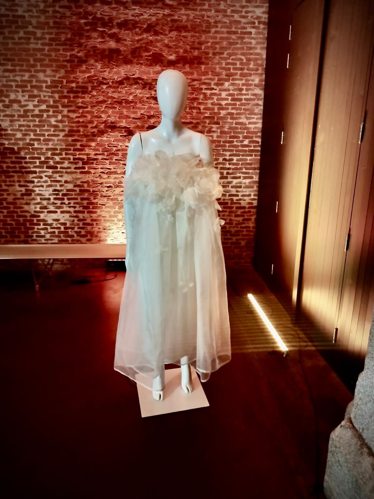 Un maniquí con un vestido blanco está parado frente a una pared de ladrillos.