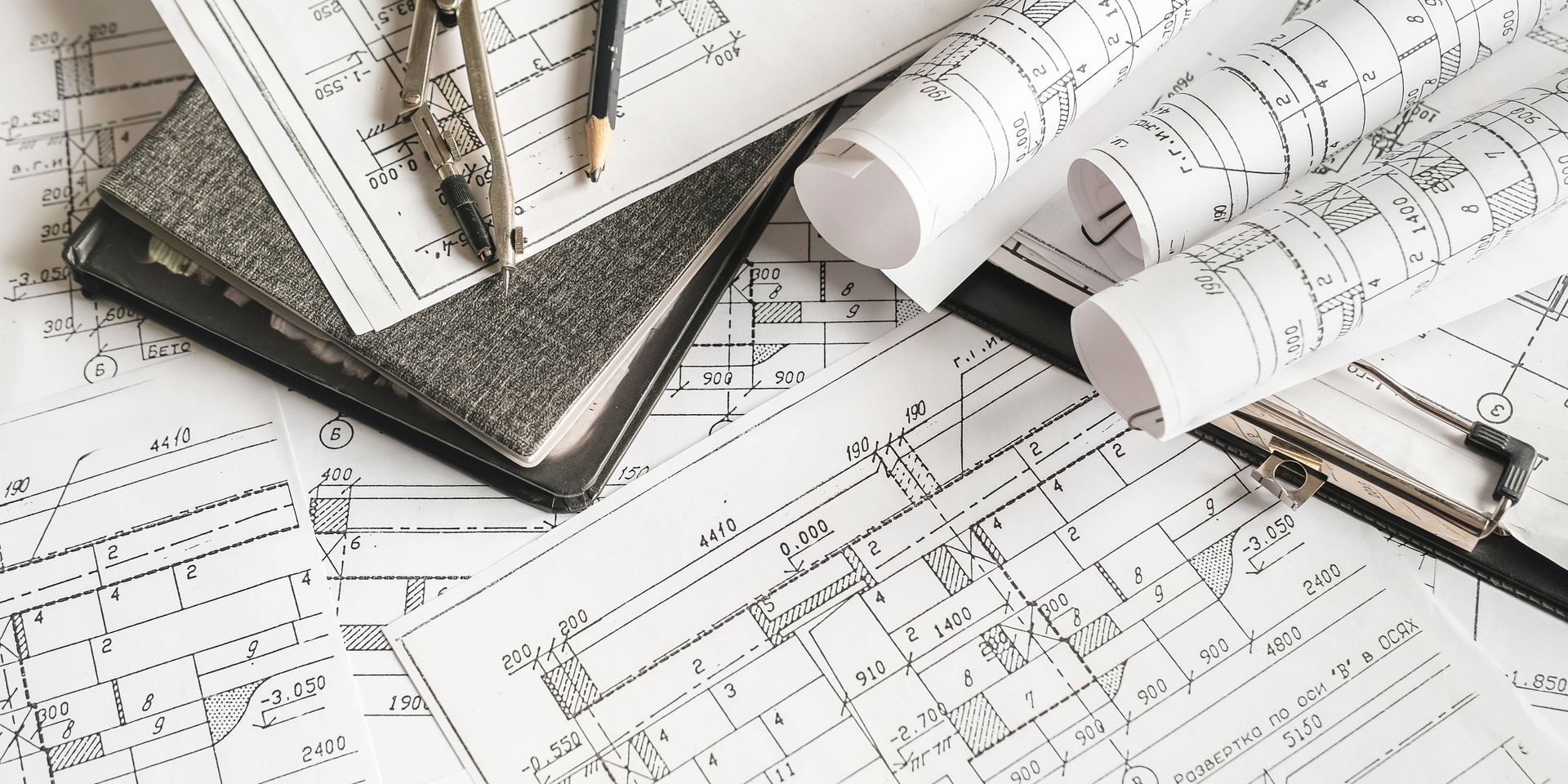 Plans architecturaux enroulés, compas, crayon et classeur sur un bureau.