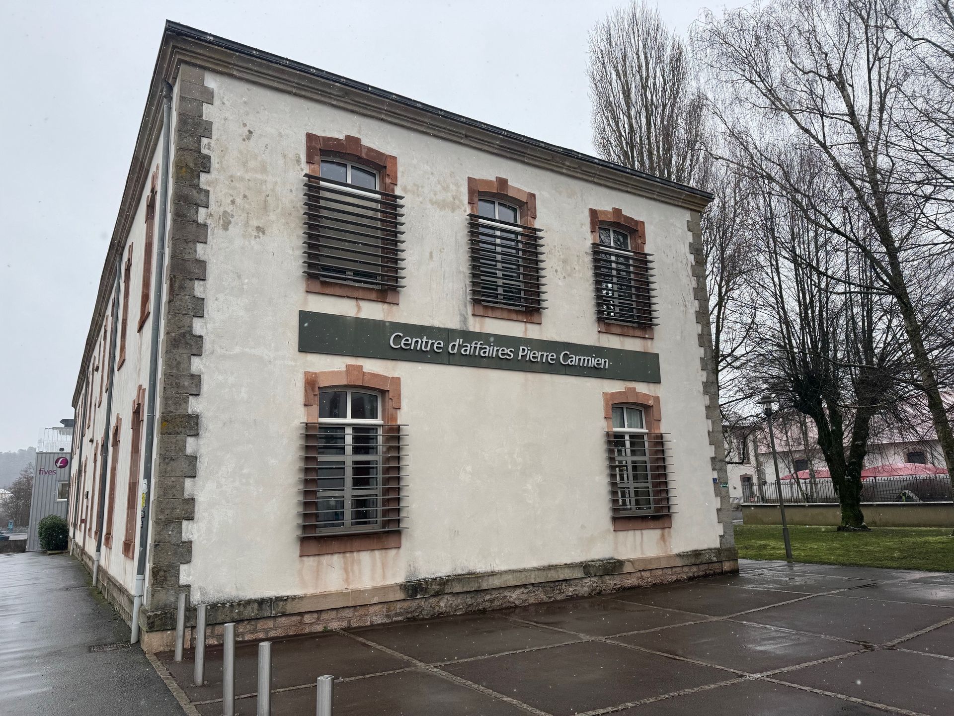 Bâtiment blanc de deux étages avec des boiseries, des fenêtres et une enseigne brunes, dans un ciel couvert.