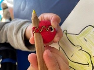 Kinderhände halten einen Buntstift, welcher an einem Ball befestigt ist, welcher zum Ausmalen hilft