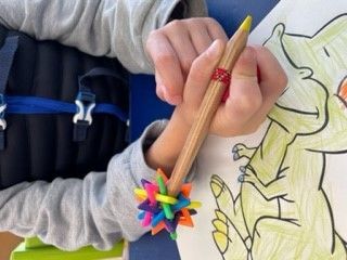 Ein buntes Gegengewicht ist hinten an einem Buntstift, welches von einem Kind beim Ausmalen gehalten wird.