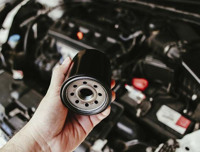 Una mano sostiene un filtro de aceite negro frente al compartimento del motor.