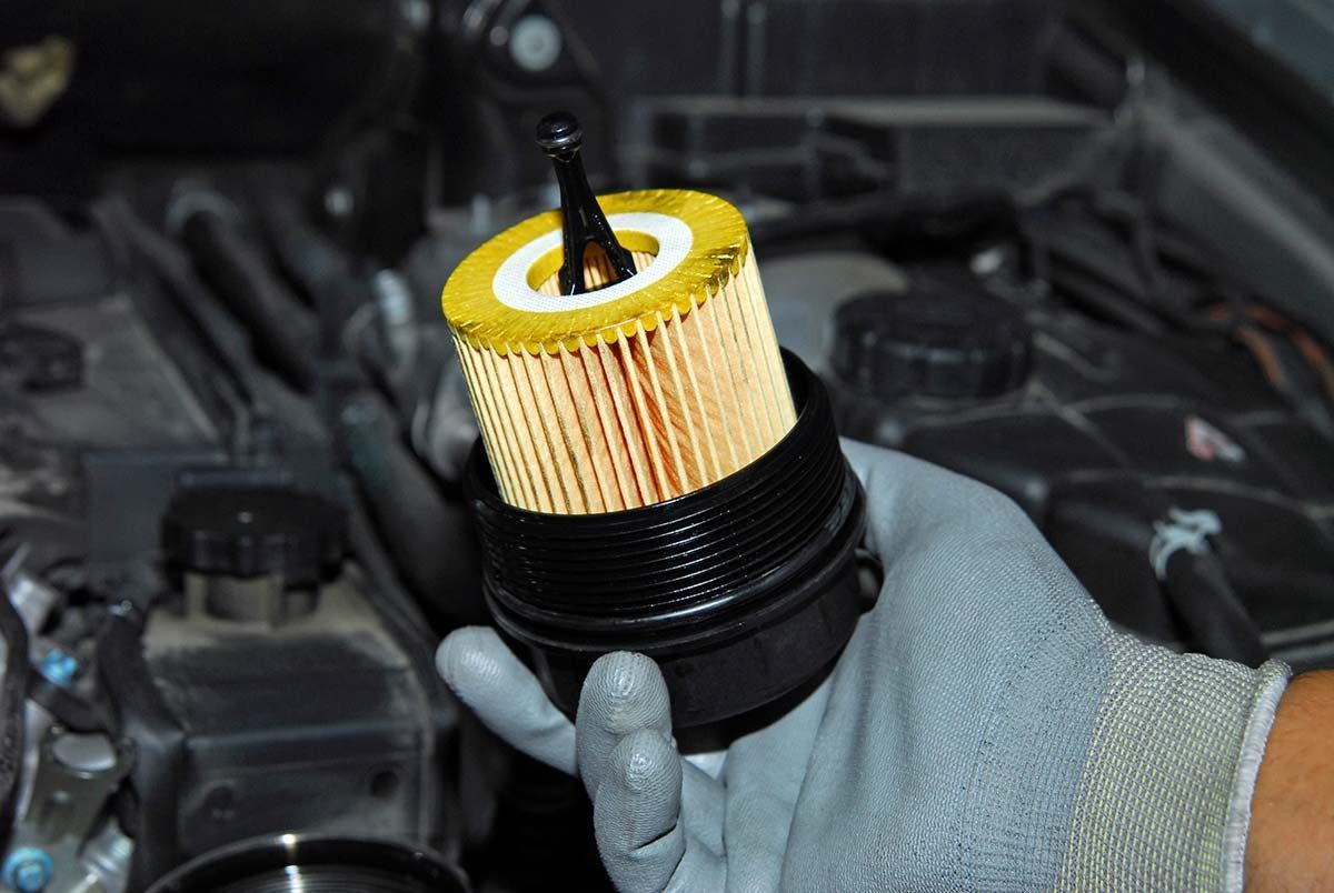 Una mano enguantada sostiene un filtro de aceite amarillo usado sobre el compartimento del motor.