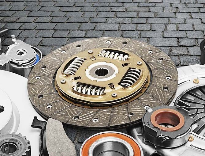 Primer plano de un conjunto de embrague y piezas metálicas dispuestas sobre adoquines al aire libre.