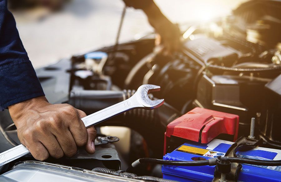 Una mano usa una llave inglesa para reparar el motor de un coche con la batería y las herramientas debajo del capó.