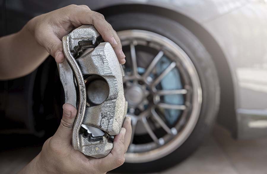 Mano sosteniendo una pastilla de freno desgastada delante de una rueda y un neumático de coche.