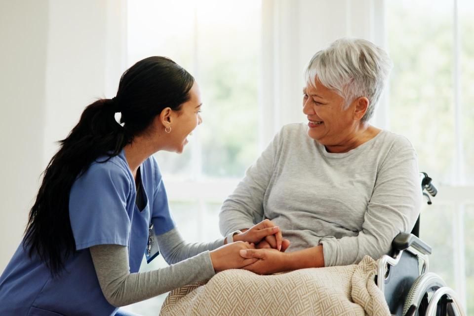 Eine Krankenschwester hält die Hand einer älteren Frau im Rollstuhl