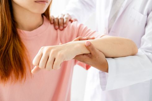 Ein Arzt untersucht das Handgelenk und den Arm einer Frau.