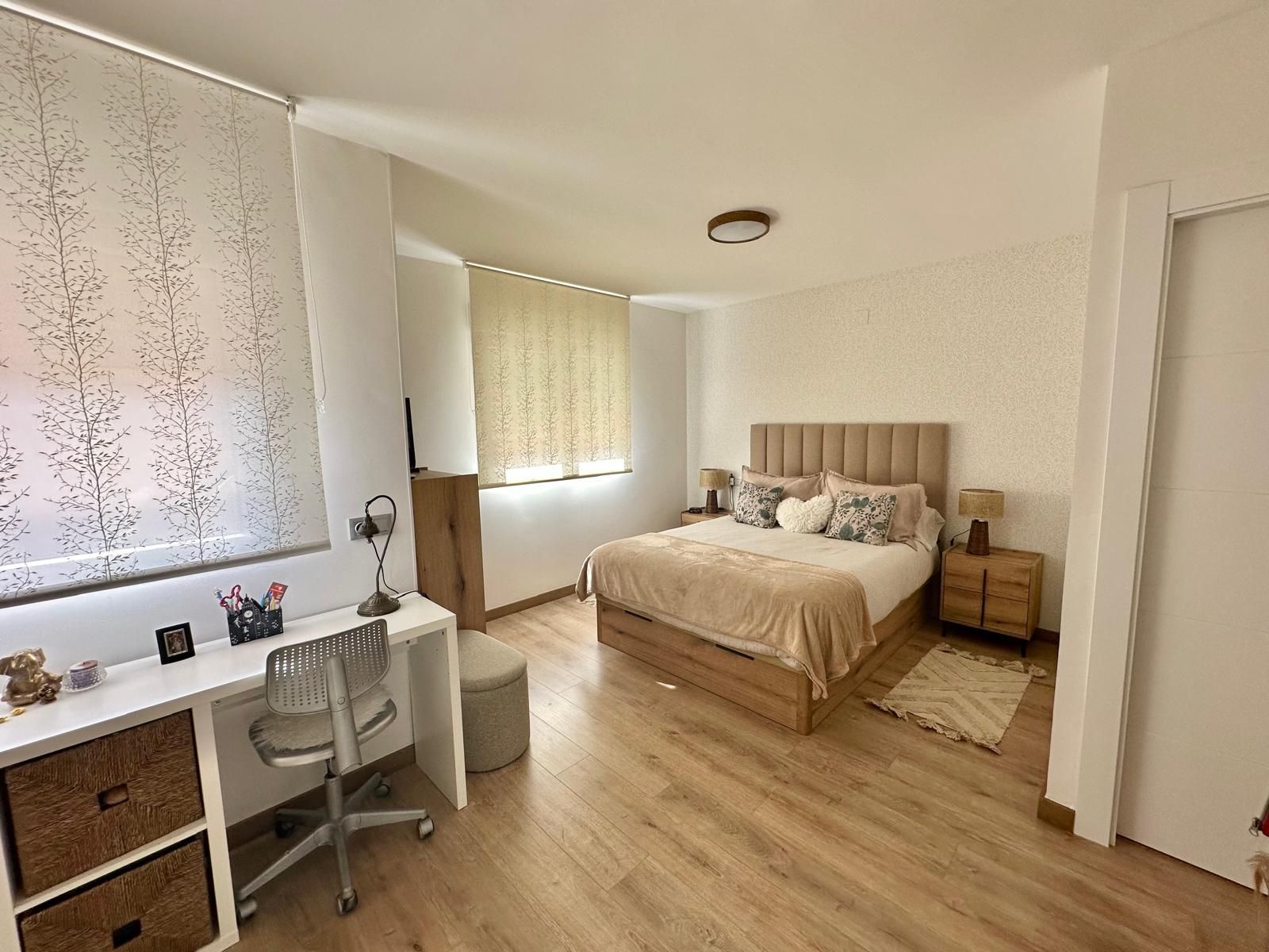 Dormitorio con escritorio, cama y mesita de noche; suelo de madera y paredes beige.
