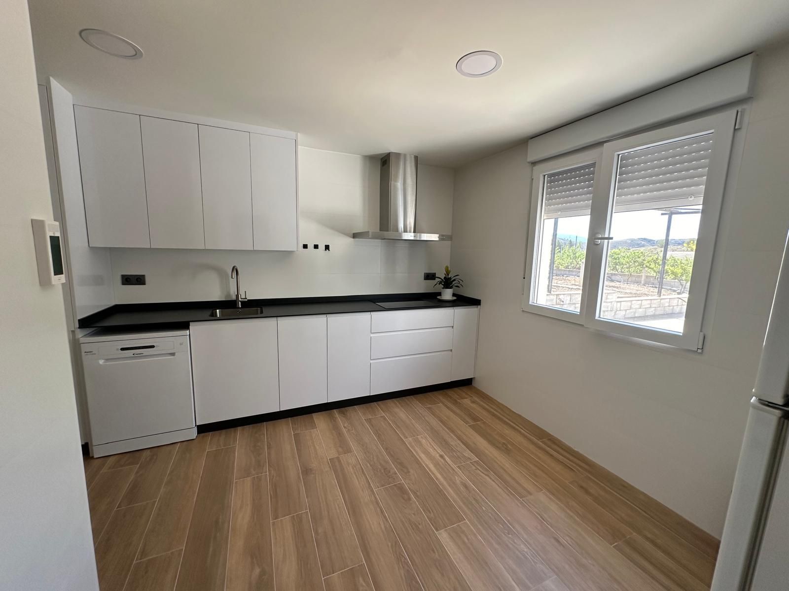 Cocina blanca con encimera, armarios y lavavajillas negros. Ventana a la derecha.