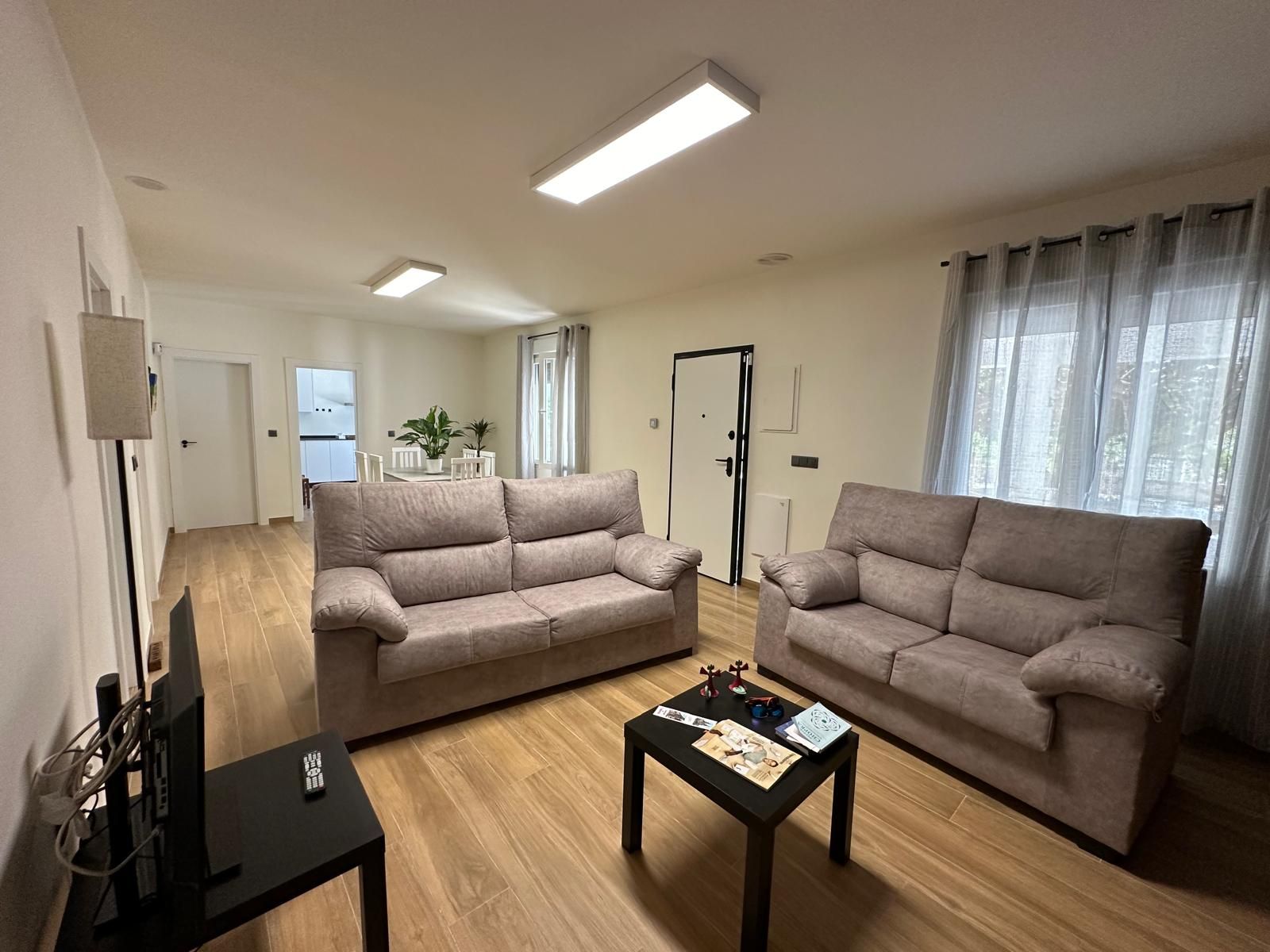 Sala de estar con dos sofás beige, mesa de centro, televisión y entrada.