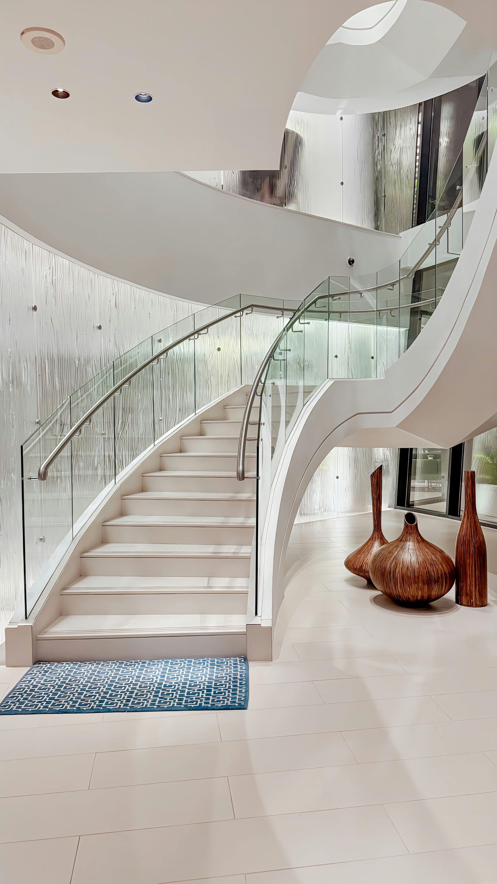 Escalera blanca moderna con barandillas de cristal y jarrones decorativos.