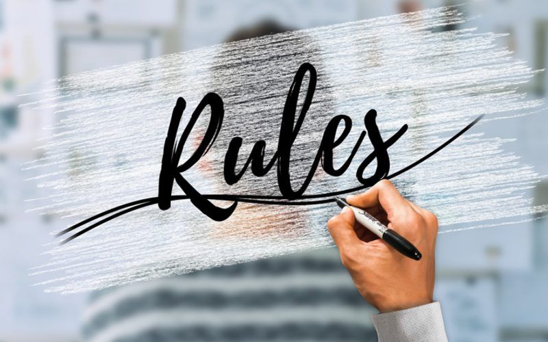 Eine Person schreibt mit einem Marker das Wort „Regeln“ auf eine Glastafel.