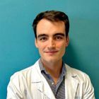 Un hombre con bata blanca sonríe, con un fondo turquesa.