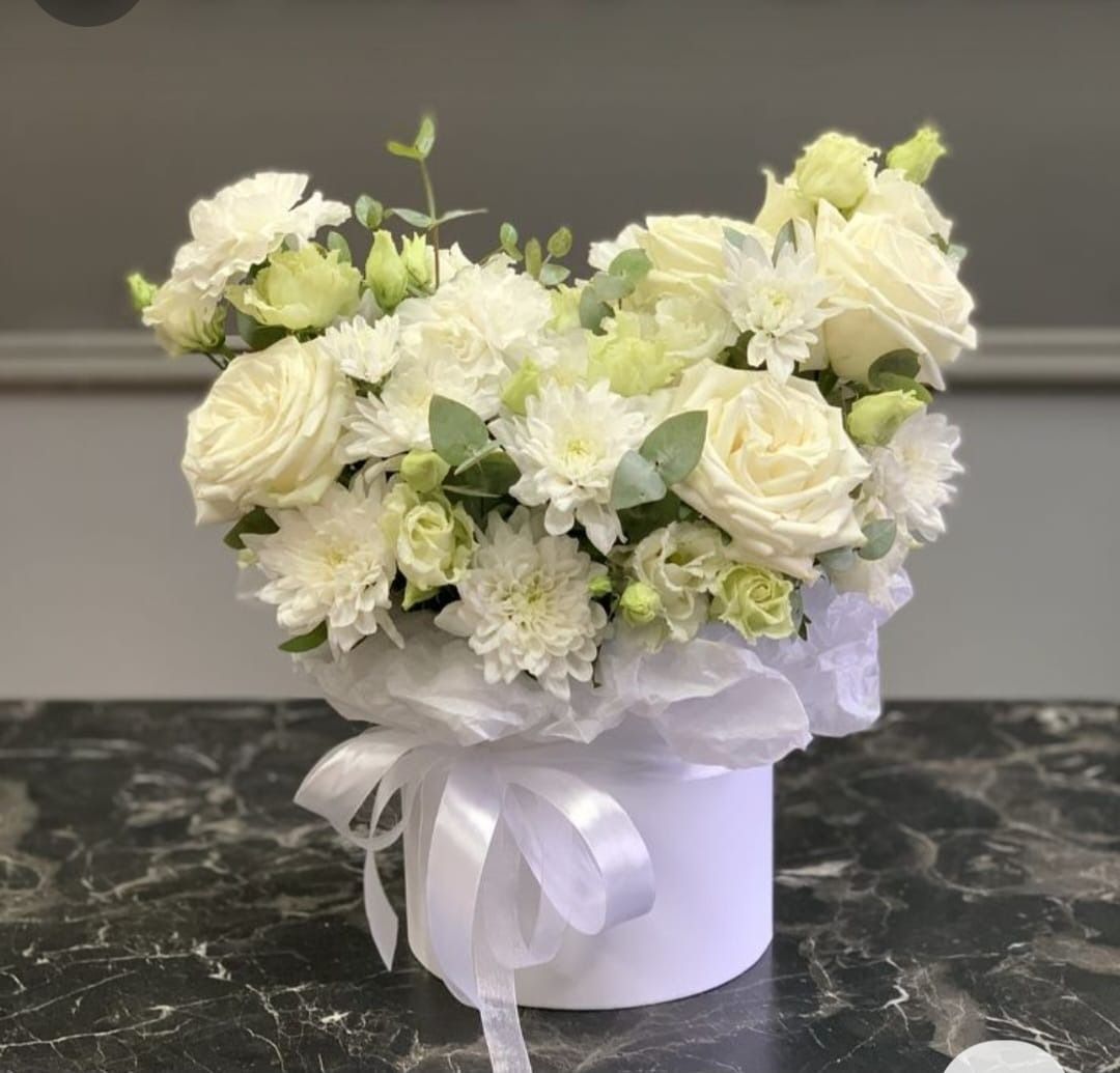 Un jarrón blanco lleno de flores blancas está sobre una mesa.